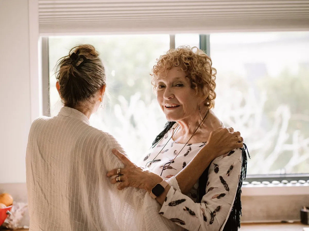 A support worker sitting with an older woman in a sunlit lounge room